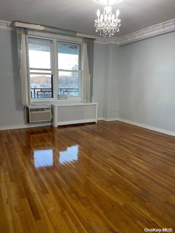 empty room with a wall unit AC, radiator, a chandelier, and dark wood-type flooring