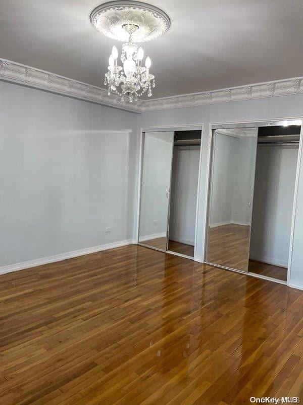 unfurnished bedroom featuring multiple closets, ornamental molding, dark hardwood / wood-style floors, and a notable chandelier