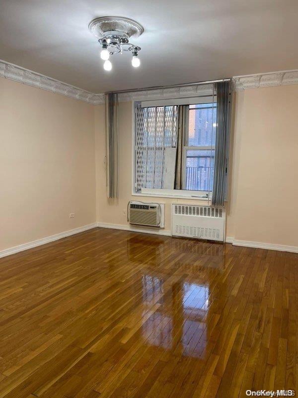 empty room featuring wood-type flooring, crown molding, radiator, and a wall mounted AC