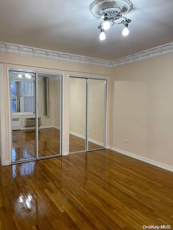 unfurnished bedroom featuring hardwood / wood-style floors, two closets, a wall mounted AC, and ornamental molding