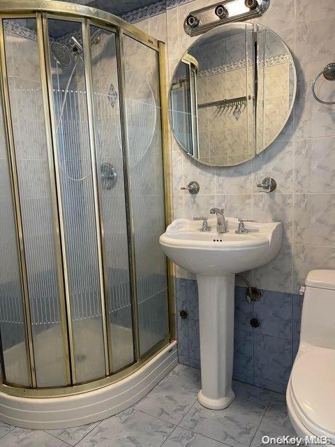 bathroom with a shower with shower door, tile walls, and toilet