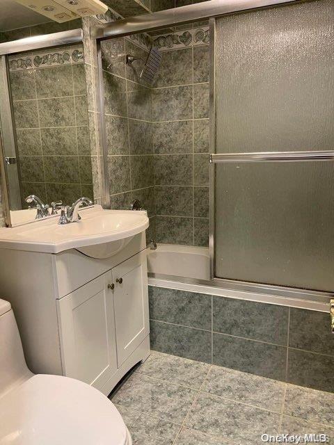 full bathroom featuring combined bath / shower with glass door, vanity, and toilet