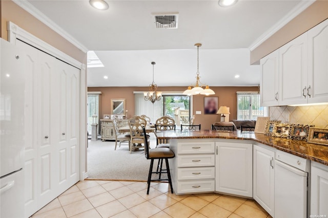 kitchen with white cabinetry, dark stone countertops, pendant lighting, light colored carpet, and ornamental molding