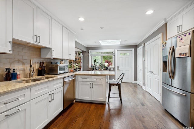 kitchen with white cabinetry, kitchen peninsula, stainless steel appliances, and a skylight