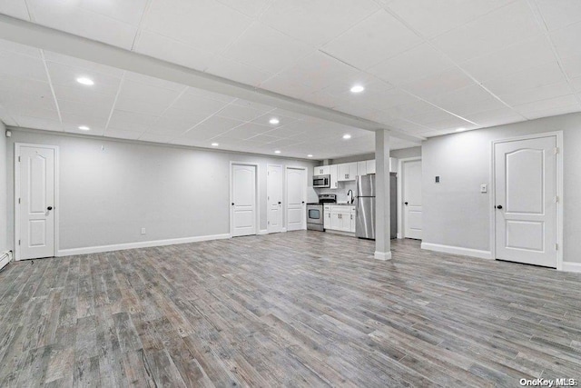 basement with light wood-type flooring, stainless steel refrigerator, and a paneled ceiling