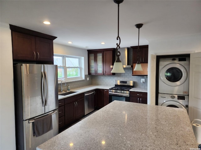 kitchen with light stone countertops, stainless steel appliances, sink, pendant lighting, and stacked washer / drying machine