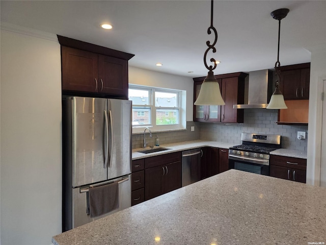 kitchen featuring light stone counters, wall chimney exhaust hood, stainless steel appliances, sink, and decorative light fixtures