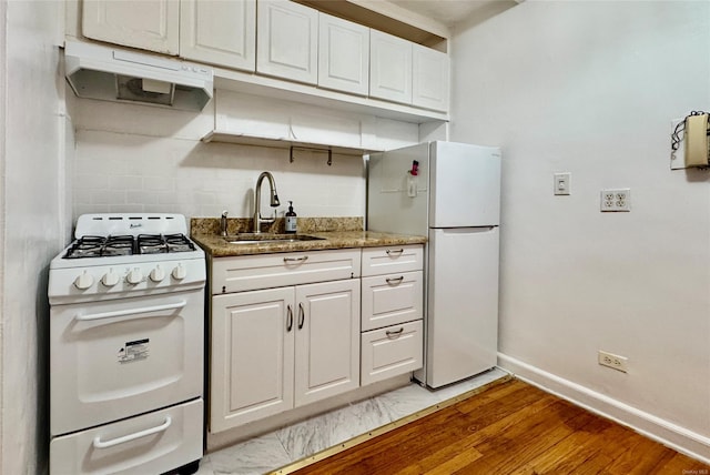 kitchen with light wood finished floors, white cabinets, a sink, white appliances, and baseboards