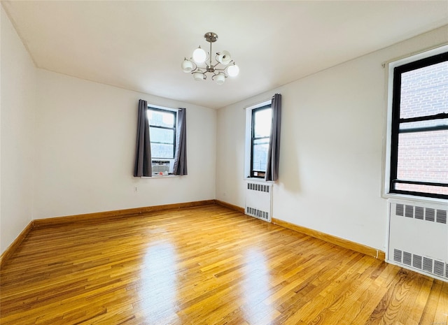 empty room featuring a chandelier, radiator, and light wood finished floors