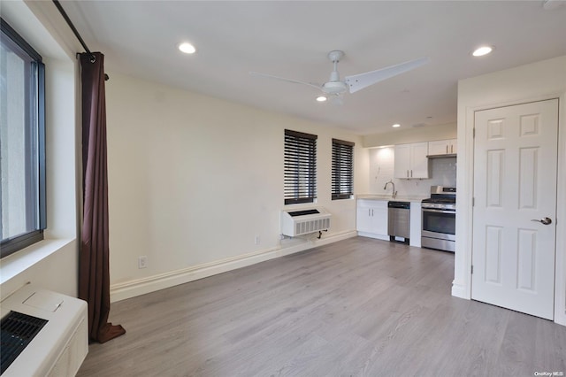 kitchen with ceiling fan, stainless steel appliances, a wall mounted AC, light hardwood / wood-style floors, and white cabinets