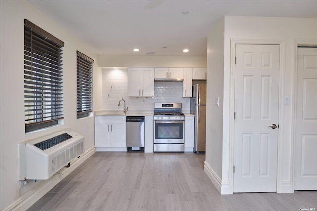 kitchen with appliances with stainless steel finishes, light wood-type flooring, backsplash, sink, and white cabinets