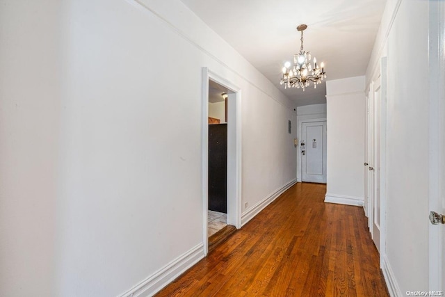 corridor with dark wood-type flooring and a notable chandelier