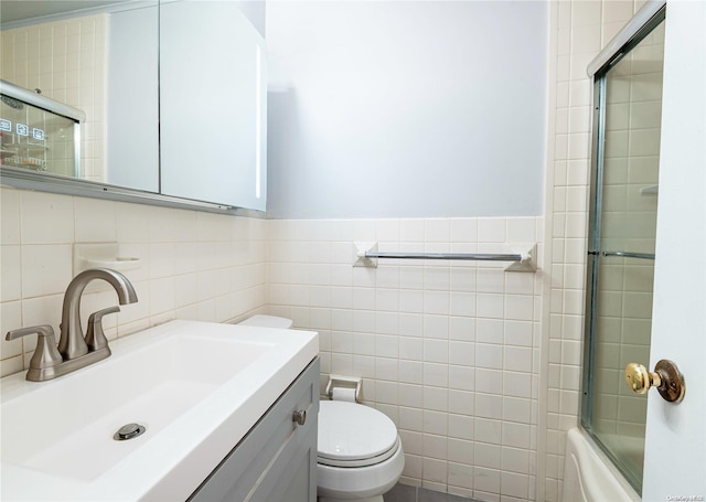 full bathroom featuring shower / bath combination with glass door, vanity, tile walls, and toilet