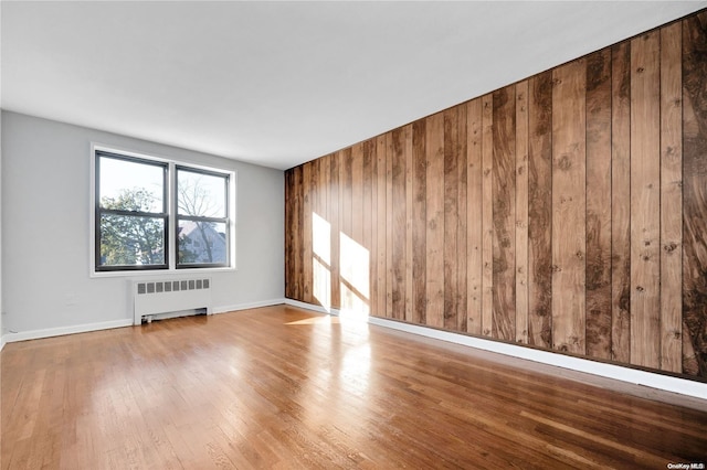 spare room featuring wood walls, light hardwood / wood-style floors, and radiator