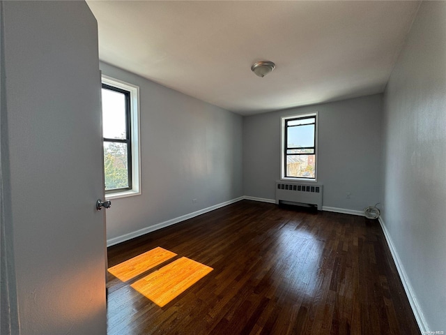 empty room featuring plenty of natural light, dark hardwood / wood-style flooring, and radiator heating unit