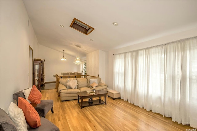 living room featuring light hardwood / wood-style floors, lofted ceiling, and a notable chandelier