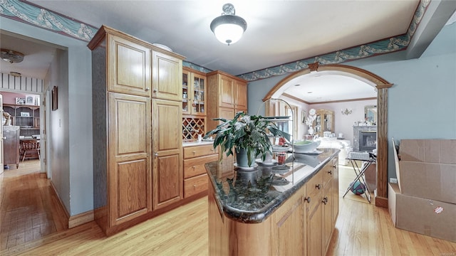 kitchen with crown molding, a center island, dark stone counters, and light hardwood / wood-style flooring