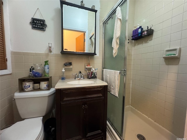 bathroom featuring a shower with door, vanity, tile walls, and toilet