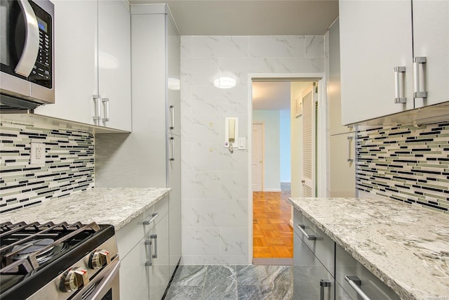 kitchen featuring white cabinets, light stone countertops, appliances with stainless steel finishes, and light parquet flooring