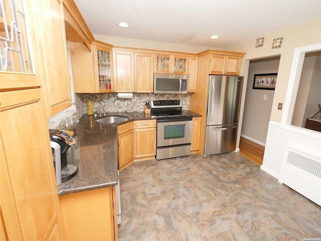 kitchen with radiator heating unit, sink, tasteful backsplash, dark stone countertops, and appliances with stainless steel finishes