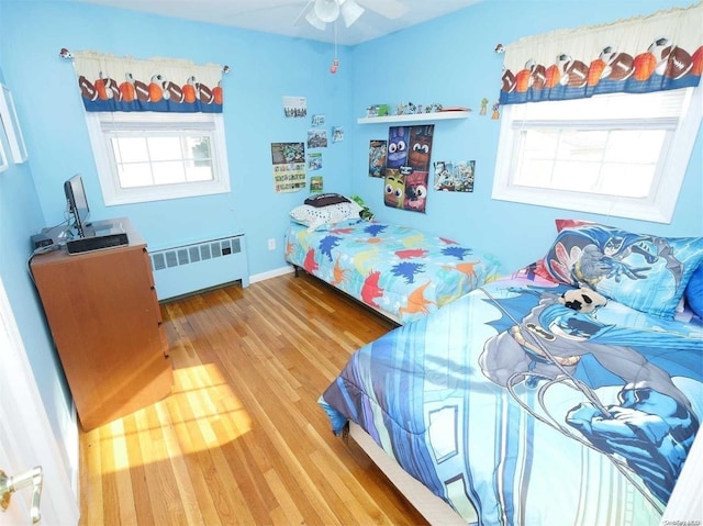 bedroom with ceiling fan, radiator heating unit, and wood-type flooring