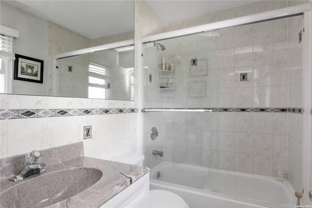 full bathroom featuring vanity, bath / shower combo with glass door, tile walls, and toilet