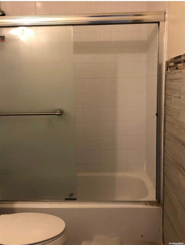 bathroom with toilet and bath / shower combo with glass door