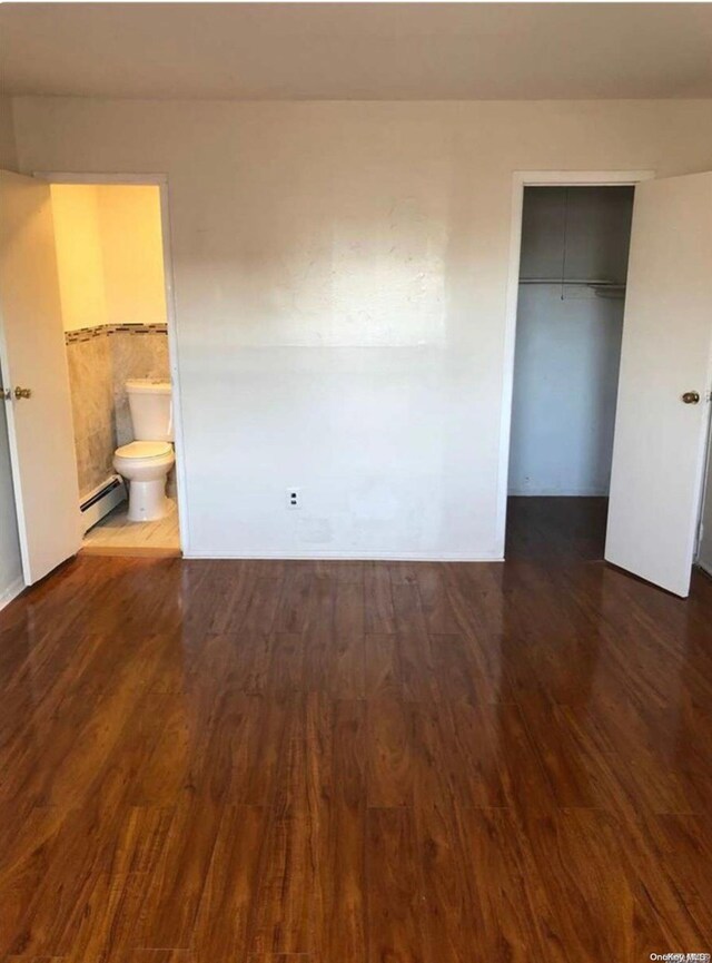 unfurnished bedroom with baseboard heating, ensuite bathroom, a closet, and dark hardwood / wood-style floors