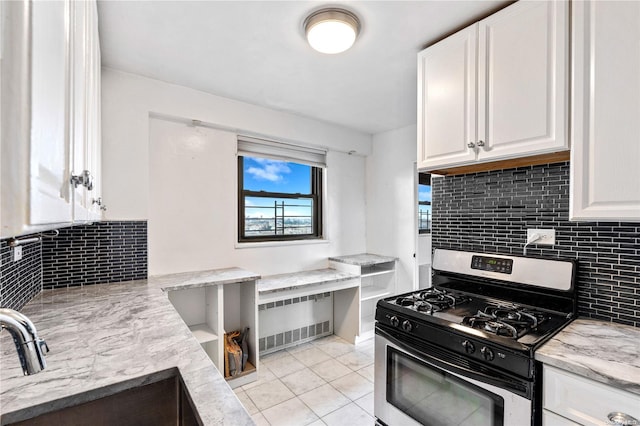 kitchen featuring white cabinetry, light stone countertops, stainless steel gas range, tasteful backsplash, and light tile patterned floors