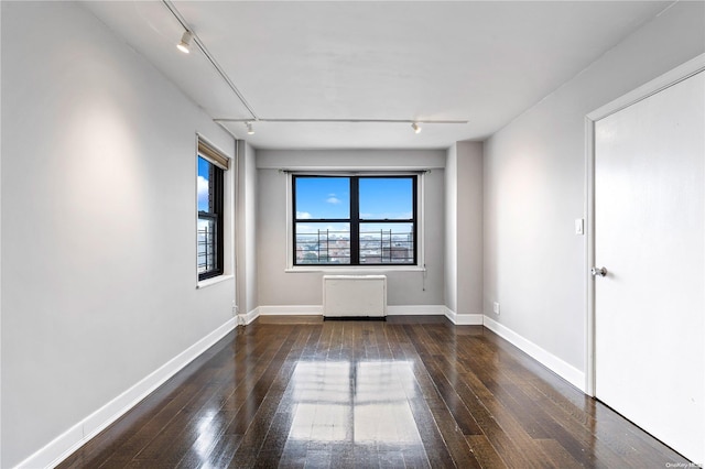 unfurnished room featuring rail lighting, radiator, and dark wood-type flooring