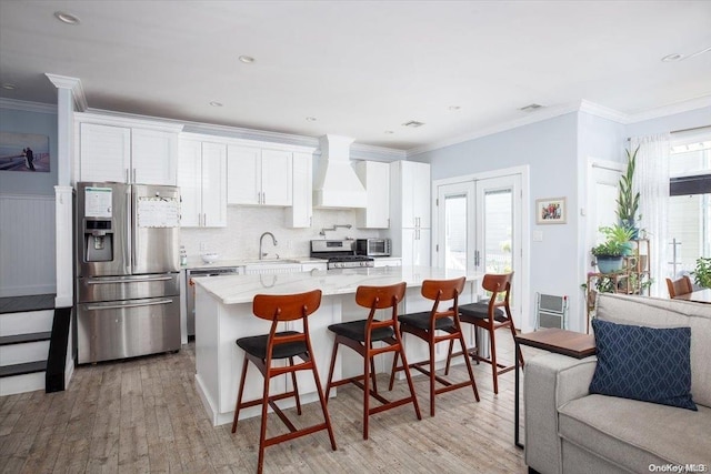 kitchen with a wealth of natural light, premium range hood, appliances with stainless steel finishes, white cabinets, and light wood-type flooring