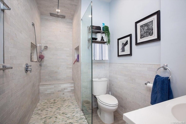 bathroom featuring tile patterned flooring, a tile shower, toilet, and tile walls