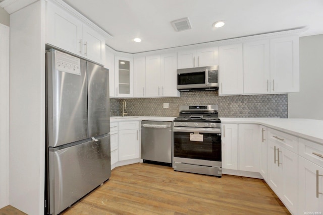 kitchen with light wood-type flooring, stainless steel appliances, white cabinetry, and tasteful backsplash