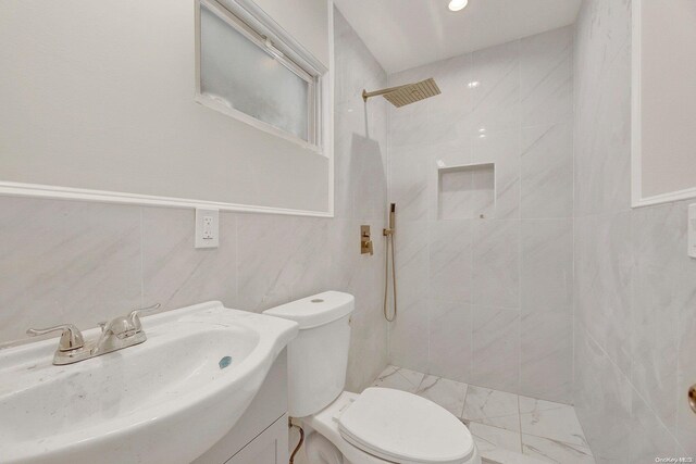 bathroom featuring vanity, toilet, a tile shower, and tile walls