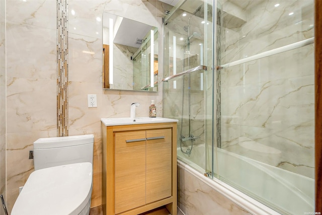 full bathroom featuring shower / bath combination with glass door, vanity, toilet, and tile walls