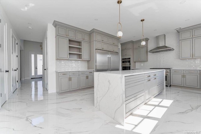 kitchen featuring high quality appliances, wall chimney range hood, hanging light fixtures, decorative backsplash, and gray cabinets