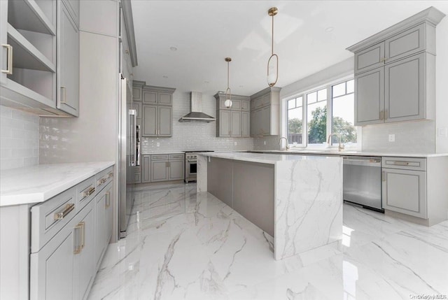 kitchen featuring decorative backsplash, appliances with stainless steel finishes, wall chimney exhaust hood, gray cabinetry, and hanging light fixtures