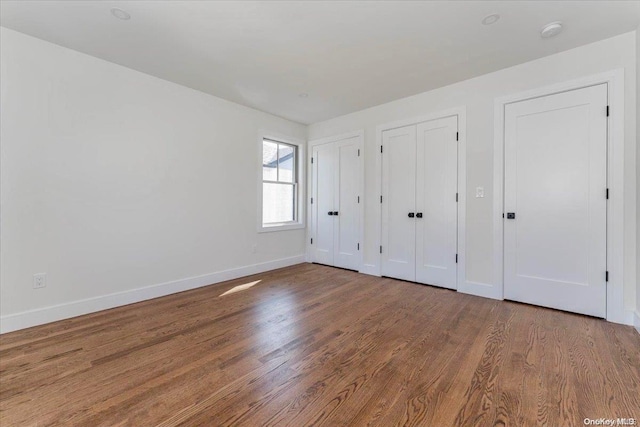 unfurnished bedroom with multiple closets and hardwood / wood-style flooring