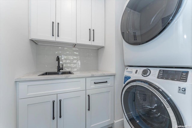 clothes washing area with cabinets, stacked washer / dryer, and sink