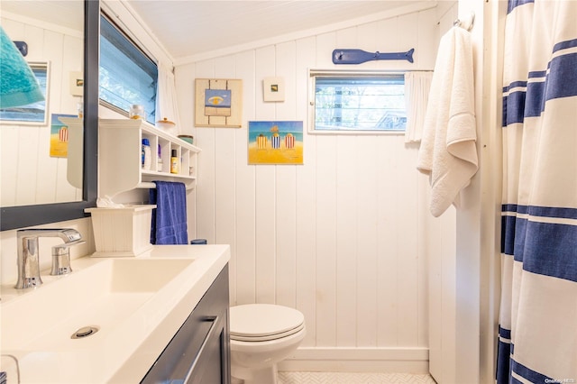 bathroom featuring vanity, wooden walls, vaulted ceiling, toilet, and ornamental molding