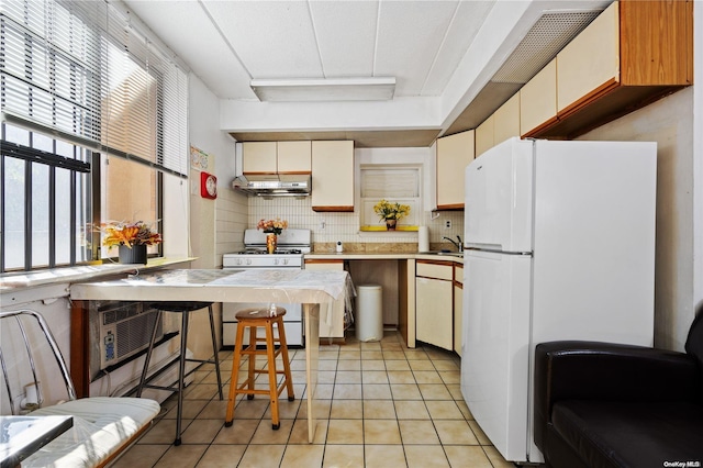 kitchen featuring sink, backsplash, white appliances, a breakfast bar, and light tile patterned flooring