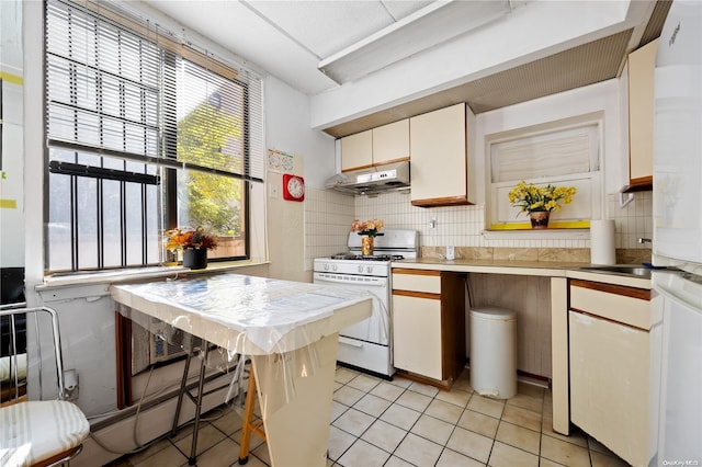 kitchen with white gas stove, sink, tasteful backsplash, light tile patterned flooring, and white cabinets