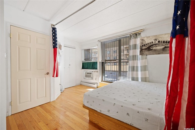 bedroom with a baseboard radiator, a wall mounted air conditioner, and hardwood / wood-style flooring