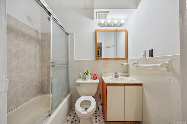 full bathroom with tile patterned floors, bath / shower combo with glass door, toilet, vanity, and tile walls