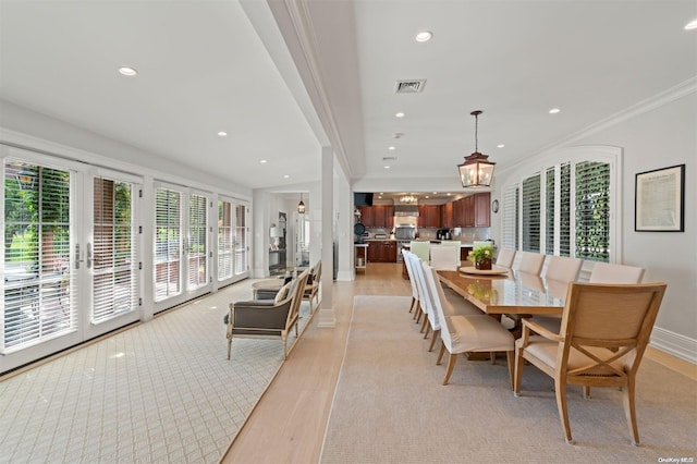 dining space with an inviting chandelier, french doors, crown molding, and light hardwood / wood-style flooring