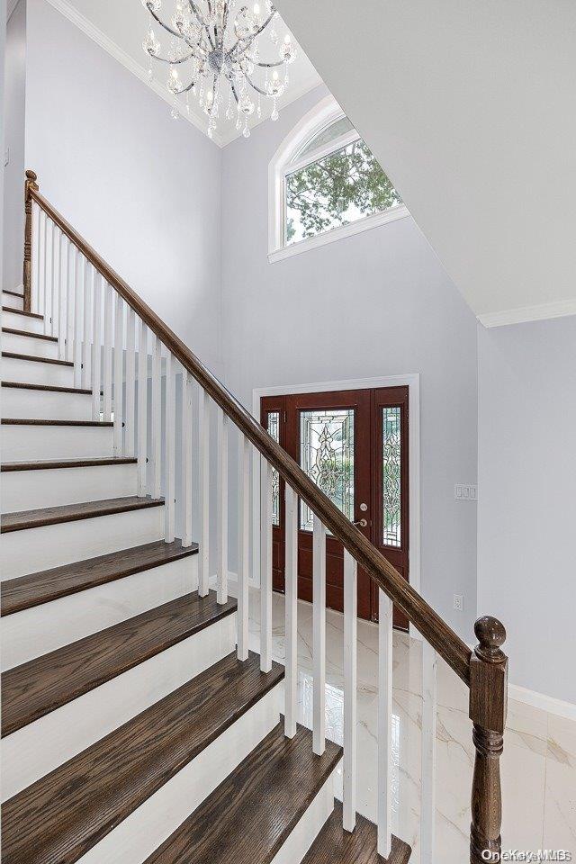 stairs featuring an inviting chandelier and crown molding