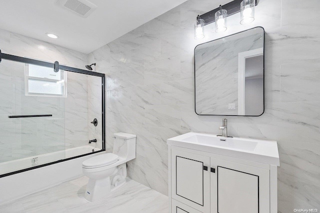 full bathroom featuring vanity, toilet, bath / shower combo with glass door, and tile walls