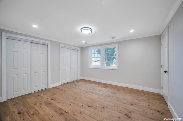 unfurnished bedroom with light wood-type flooring, crown molding, and multiple closets