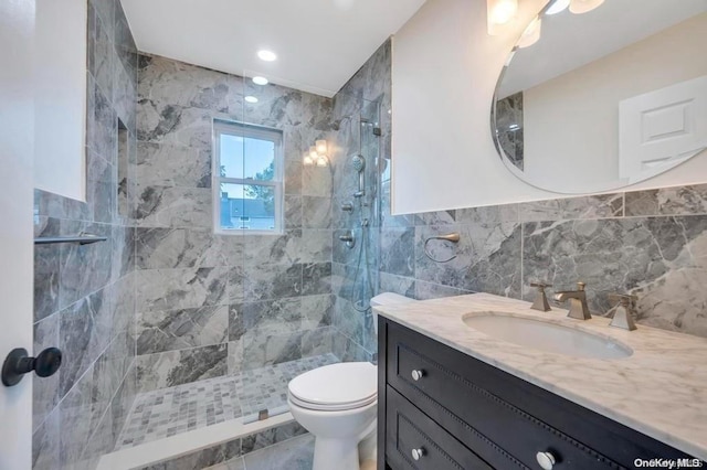 bathroom featuring a tile shower, vanity, tile walls, and toilet