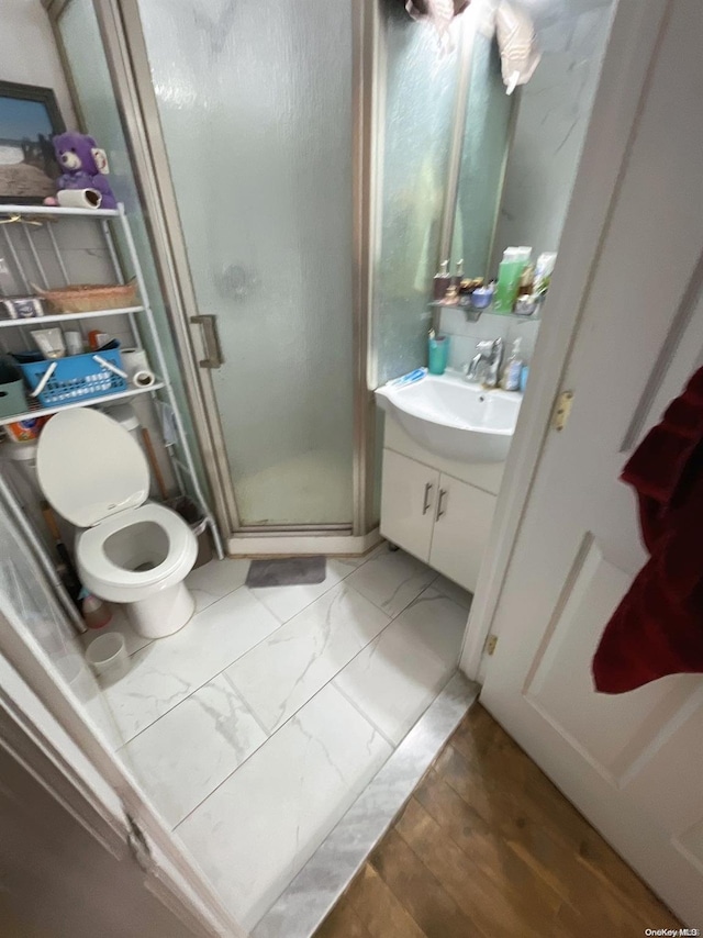 bathroom with wood-type flooring, vanity, toilet, and a shower with shower door